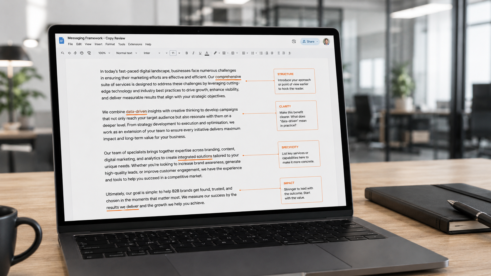 Laptop on a light wood desk in a bright modern office, displaying a full-page copy review document with orange comment boxes offering advice on structure, clarity, specificity and impact.